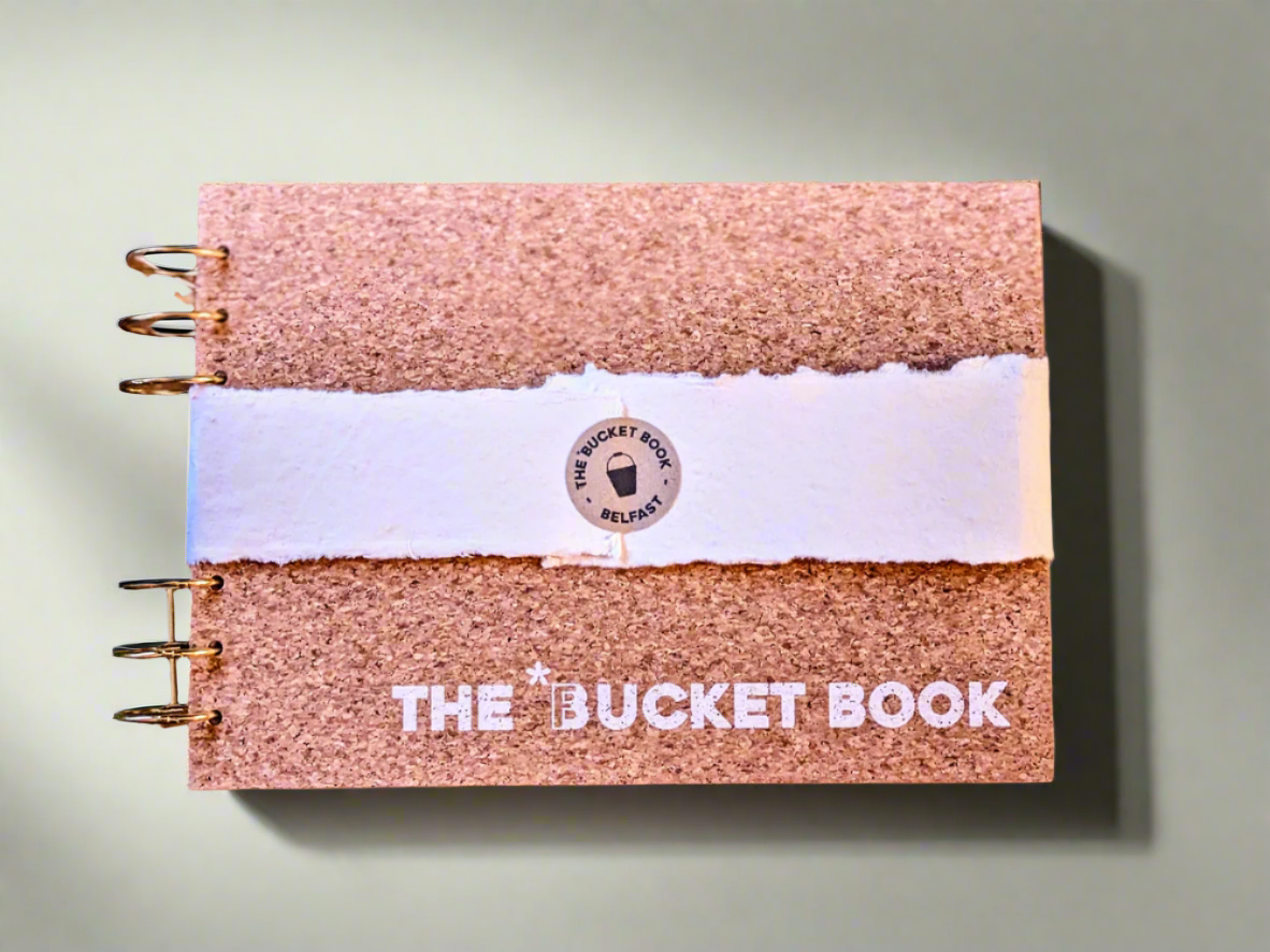 Cork-bound notebook with 'The Bucket Book' branding on a textured background